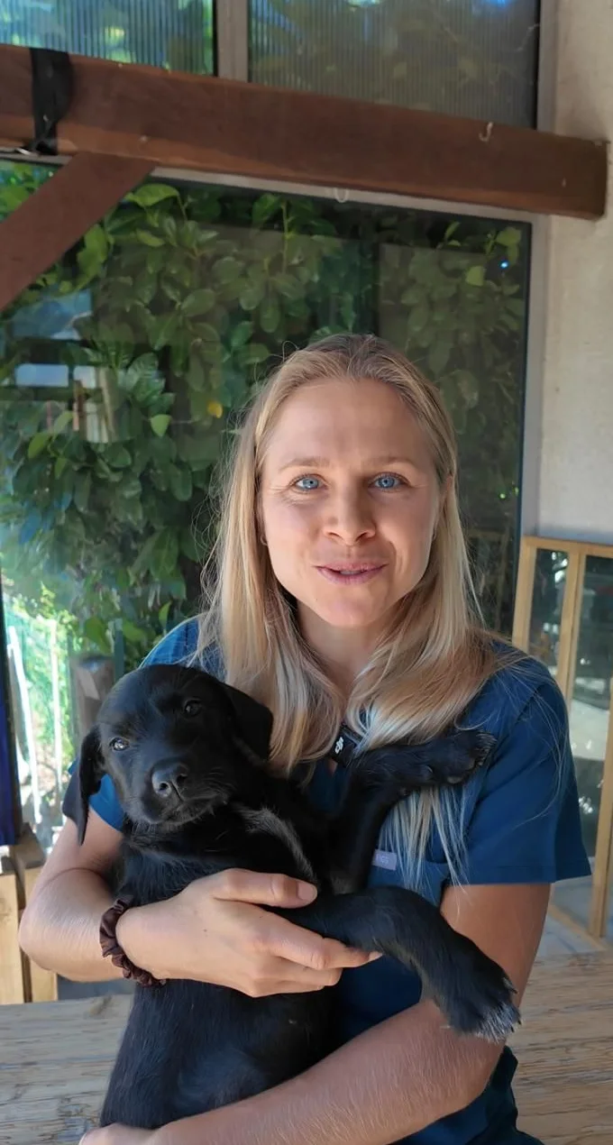 Olivia, vétérinaire, sourit en tenant un chiot noir dans ses bras