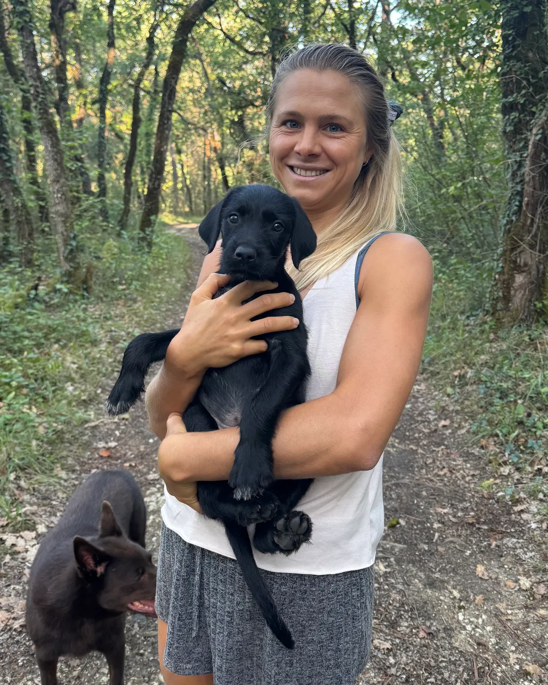 Olivia en forêt, un chiot noir blotti dans ses bras